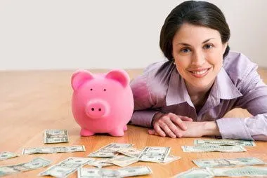 Woman lying down smiling with a piggy bank surrounded by dollar bills, representing financial happiness, savings success, and personal money management.
